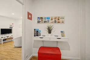 A room with a white wall, a red storage box, a white console table with books and a potted plant, and a wall-mounted photo collage. - Casa Beco Do Castelo (Lisbon)