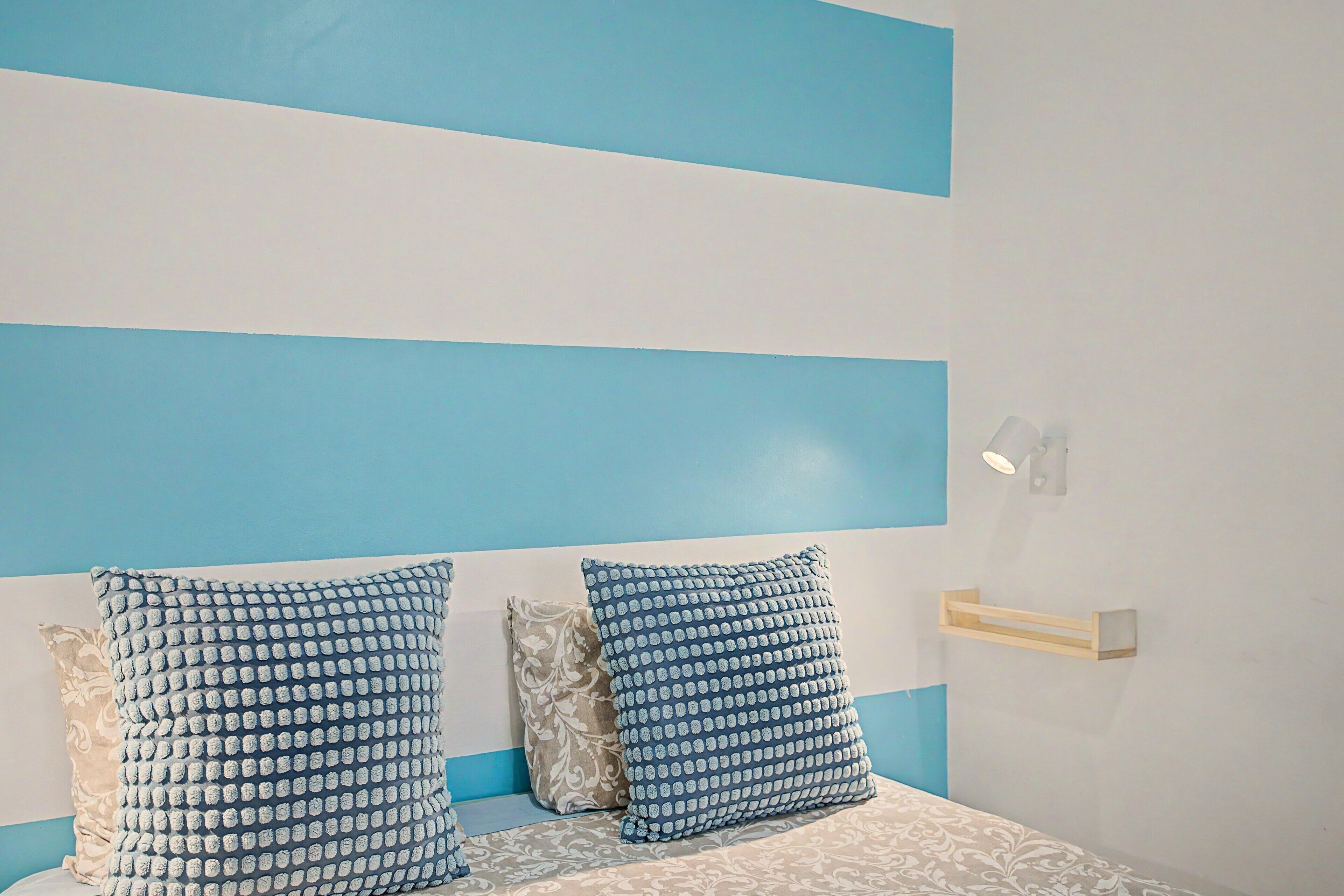 Un lit recouvert d’une couvre-lit à motifs, deux oreillers à motifs bleus et blancs, et une table de chevet avec un lampadaire.