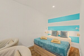 A bedroom with a bed, a chair, and a blue accent wall. - Casa Beco Do Castelo (Lisbon)