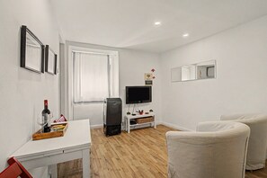 A modern living room with a flat-screen TV, a white sofa, a dining table with a wine bottle, and a small white cabinet. - Casa Beco Do Castelo (Lisbon)