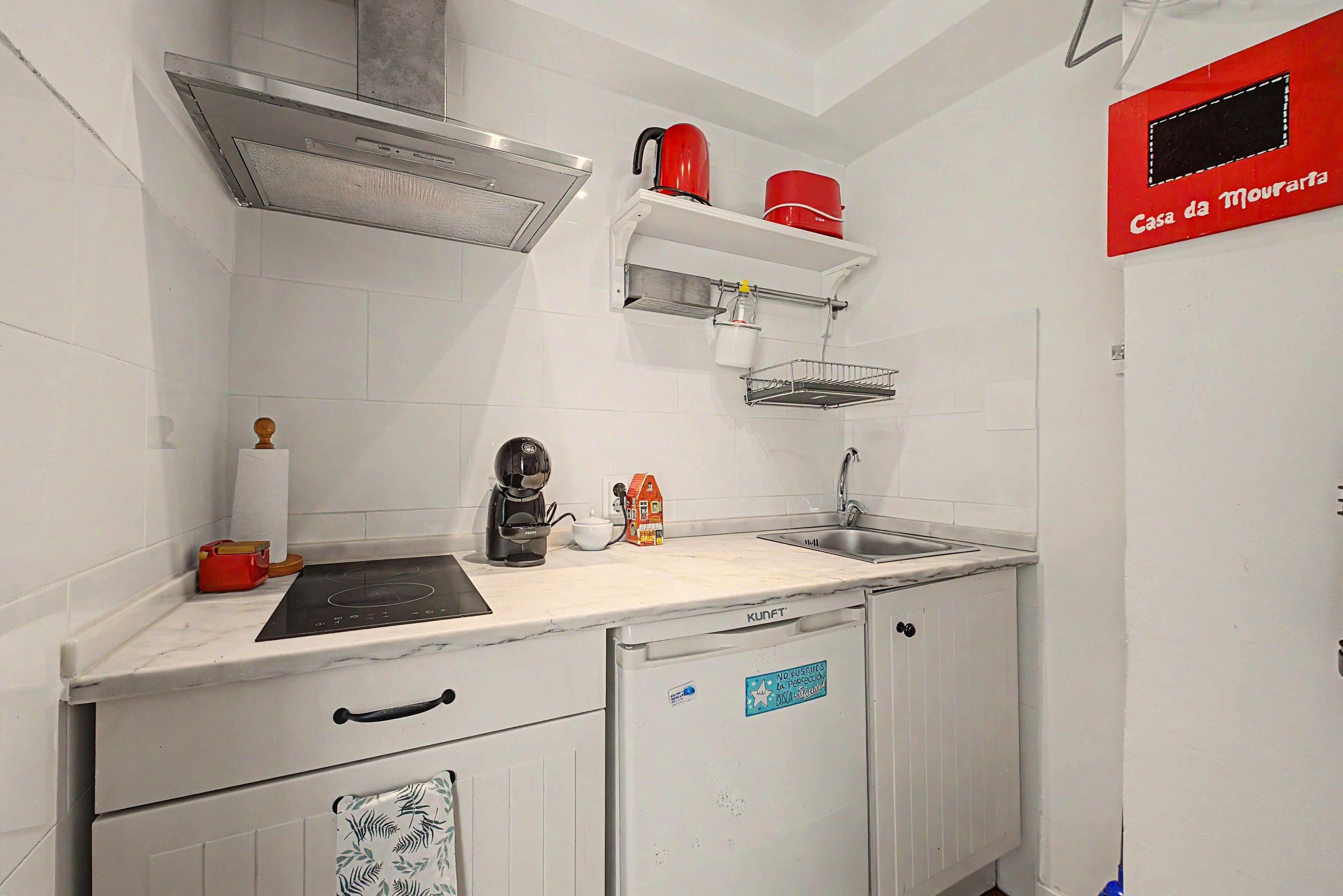 A compact kitchen with white cabinets, a stainless steel range hood, a coffee machine, and a red kettle.