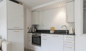 Cocina compacta con armarios blancos, encimera negra y horno empotrado.