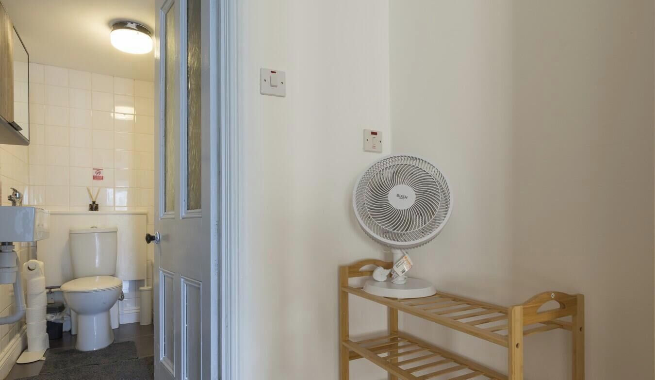 A bathroom with a toilet, a sink, a mirror, a fan, and a shelf.