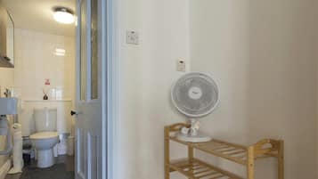 A bathroom with a toilet, a sink, a mirror, a fan, and a shelf.