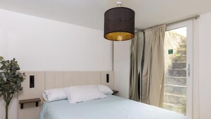 Een slaapkamer met een bed, nachtkastje, wandtelefoon, hanglamp en raam met gordijnen.