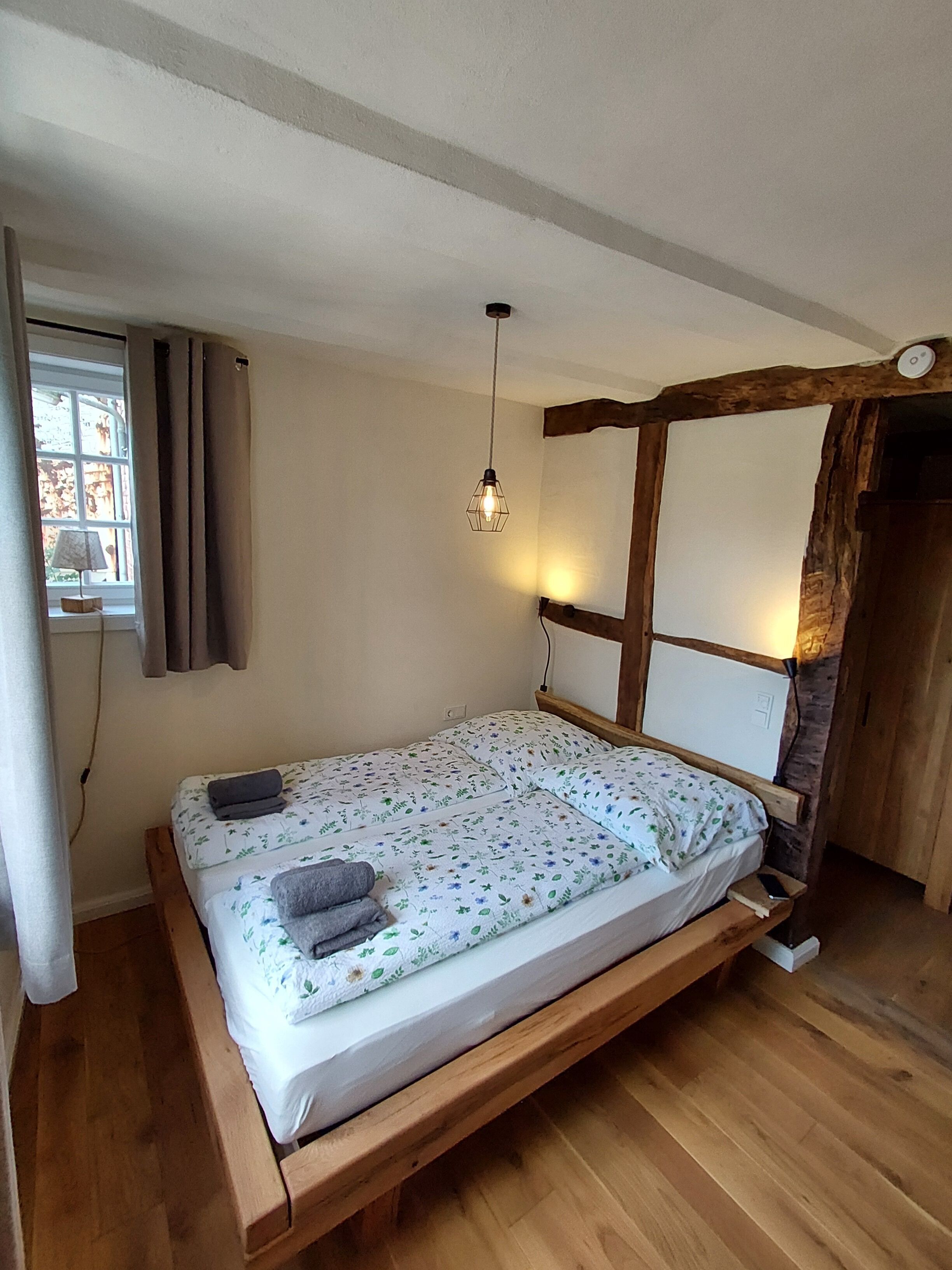 A single bed with a wooden frame, a hanging light fixture, and a window with curtains.