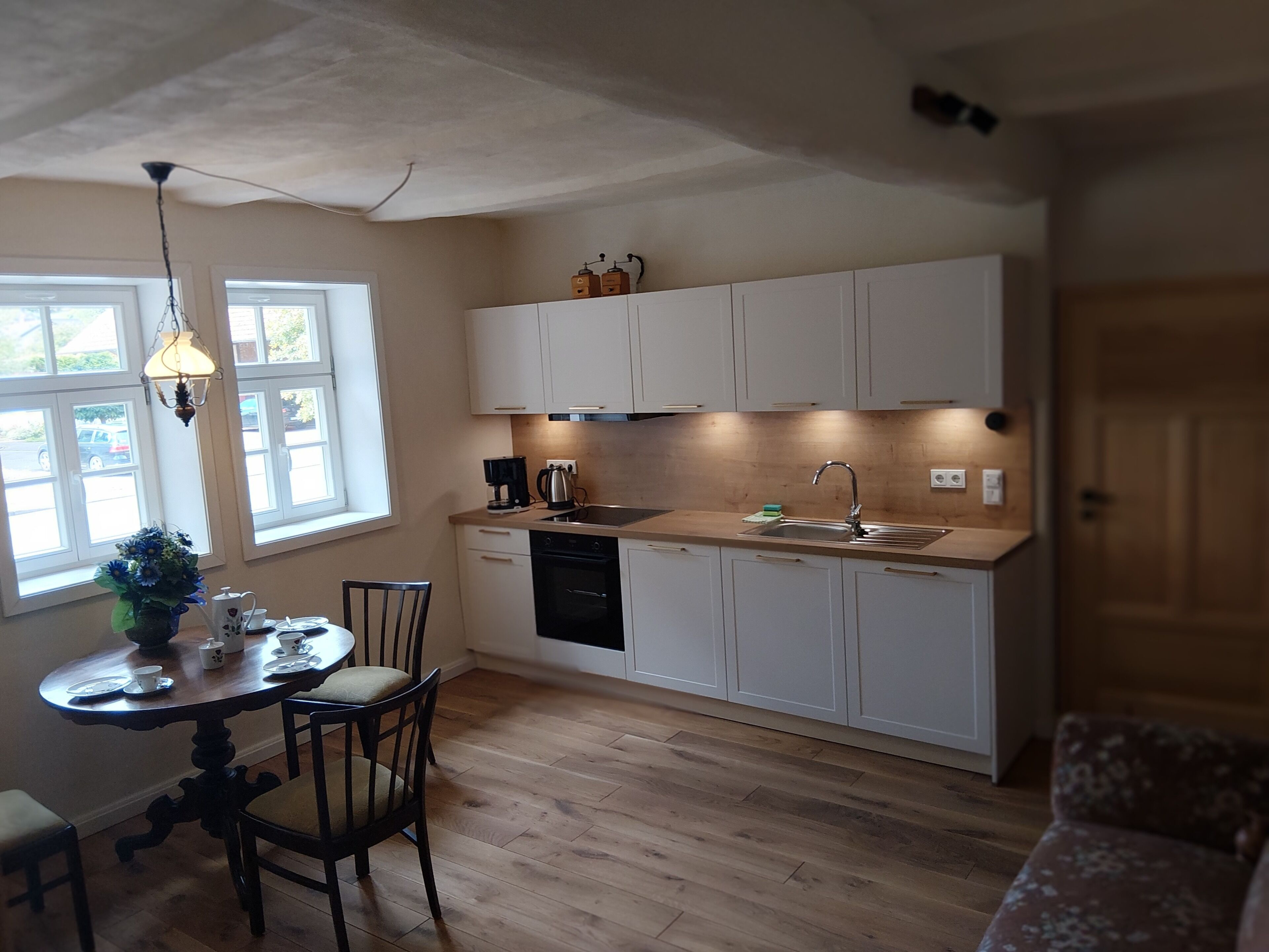 Eine kleine Küche mit weißen Schränken, einer Holz Arbeitsplatte, einem Spülbecken und einem Essbereich mit Tisch und Stühlen.