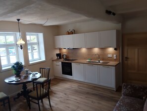 A compact kitchen with white cabinets, a wooden countertop, a sink, and a dining area with a table and chairs. - LANDHAUS ELLENBACH - Romantic Half-Timbered Charm on the Fulda River, Cozy Vacation Rental in a Historic Building (Alheim)