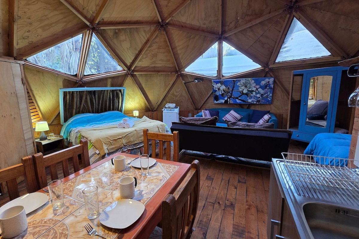 Un interior acogedor con una cama, zona de estar y una mesa de comedor preparada para dos personas.