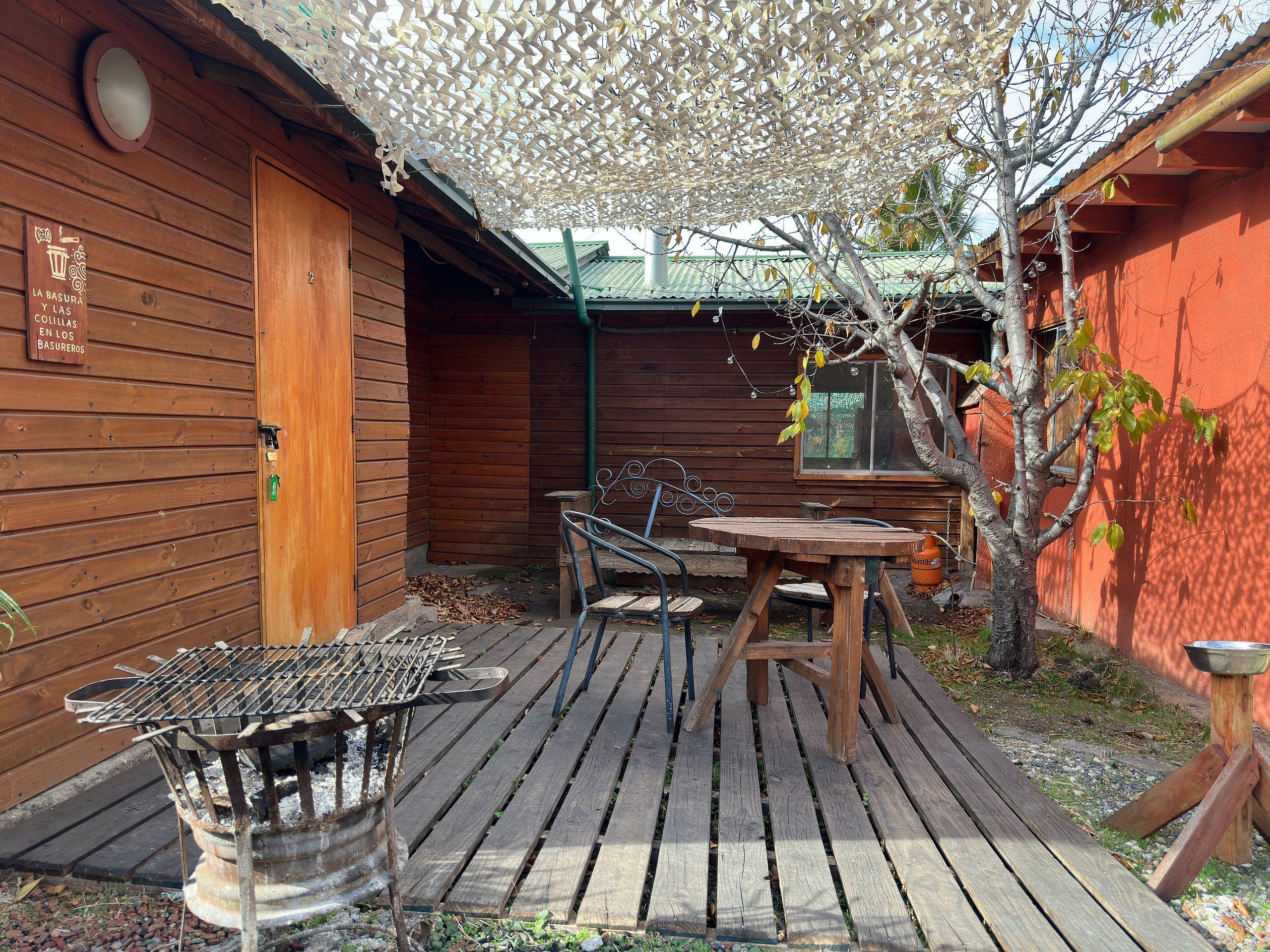 Een houten terras buiten met een barbecue, een tafel en stoelen.