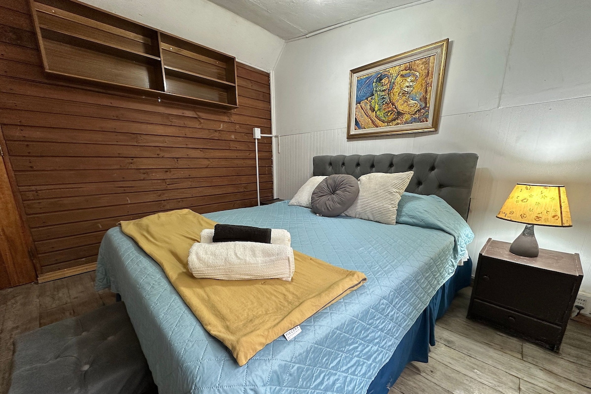Un dormitorio con una cama, una mesita de noche, un estante en la pared y un cuadro.