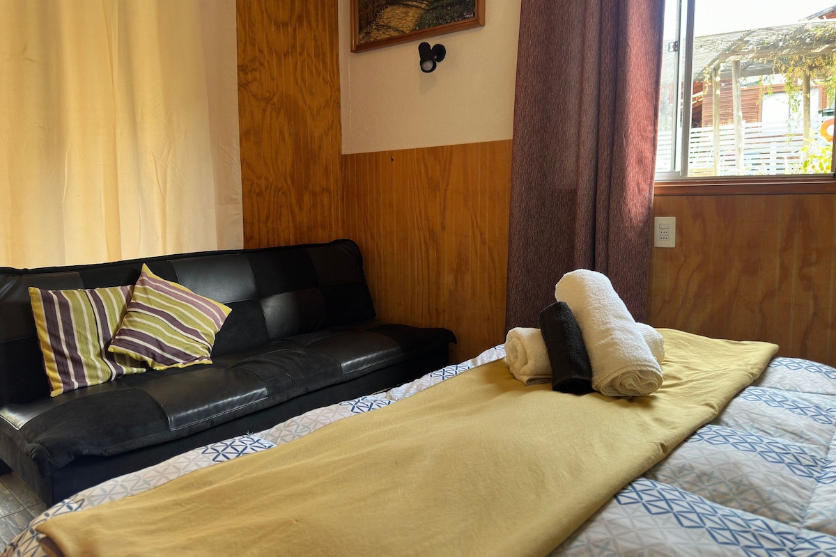 Una habitación con un sofá de cuero negro, una cama con colcha estampada y un panel de pared de madera.