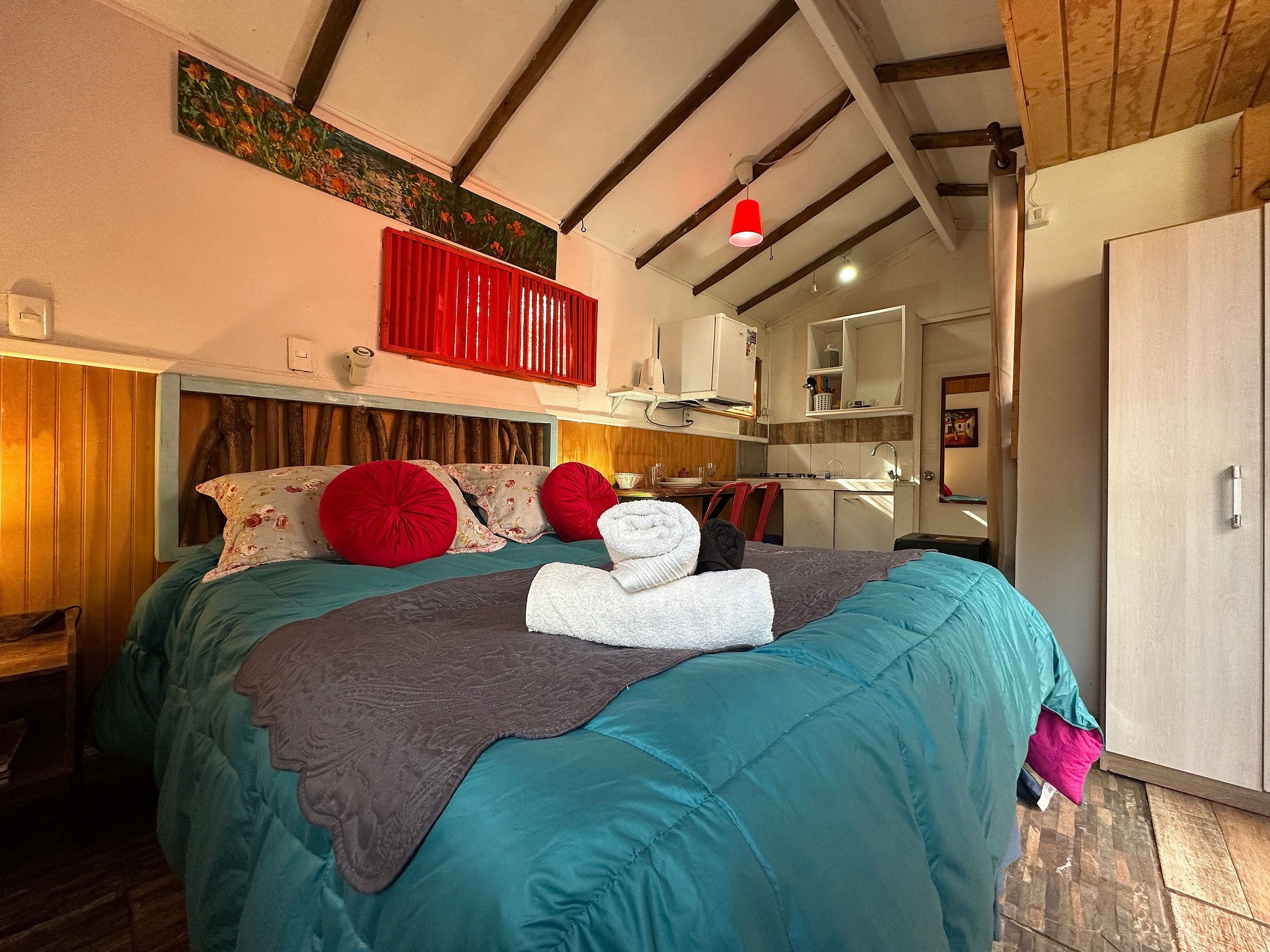 Ein Schlafzimmer mit Bett, Kissen, Decke, einem roten Kopfteil, einem Gemälde, einem Spiegel, einem Waschbecken und einem Kleiderschrank.