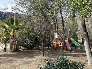 Un parque infantil con un tobogán y estructuras para escalar, rodeado de árboles.