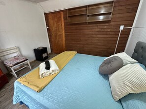 Un dormitorio con cama, una silla, un calentador y un armario.