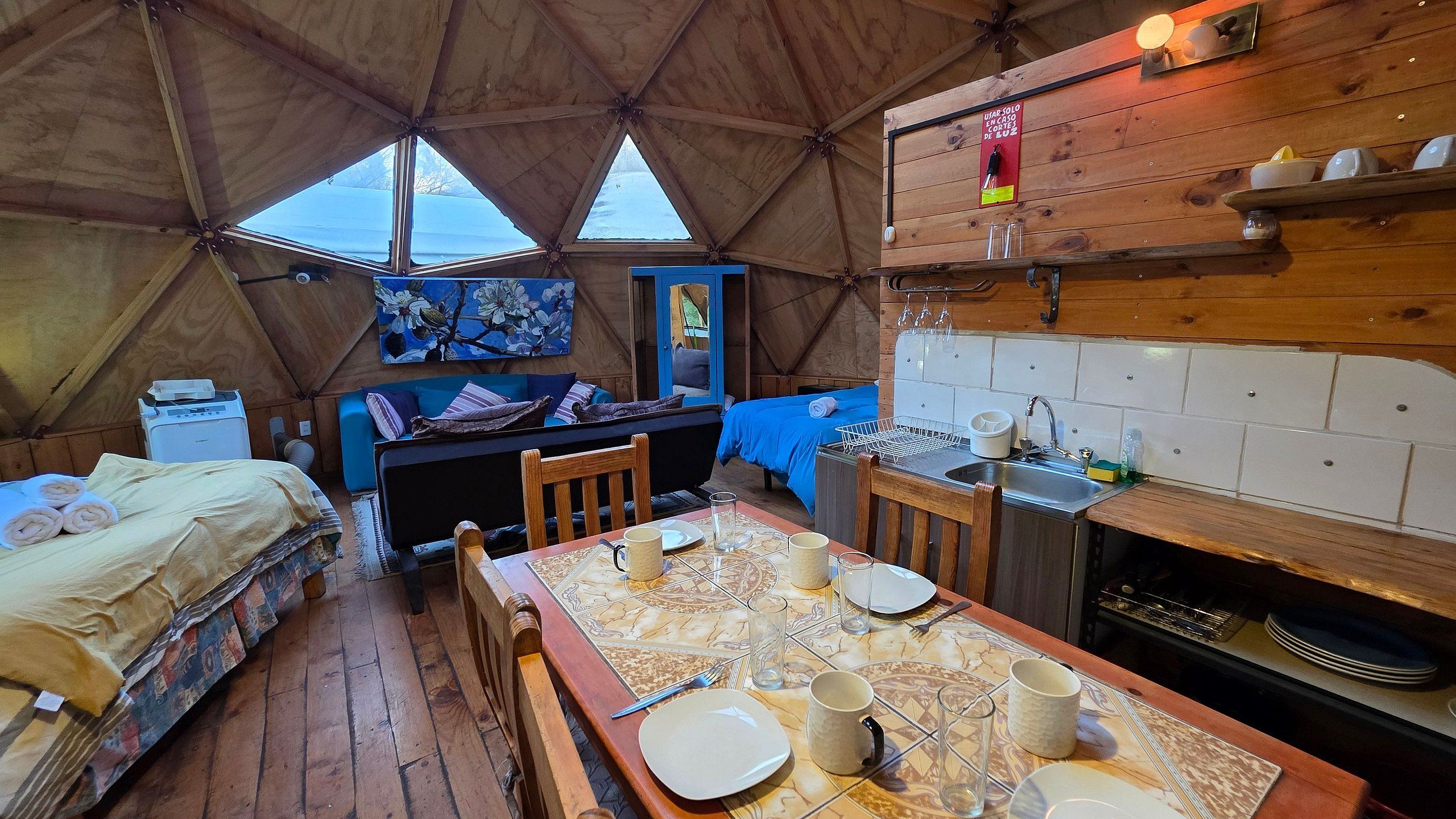 A cozy interior with a dining table set for two, a bed with a blue headboard, and a kitchen area with a stove.