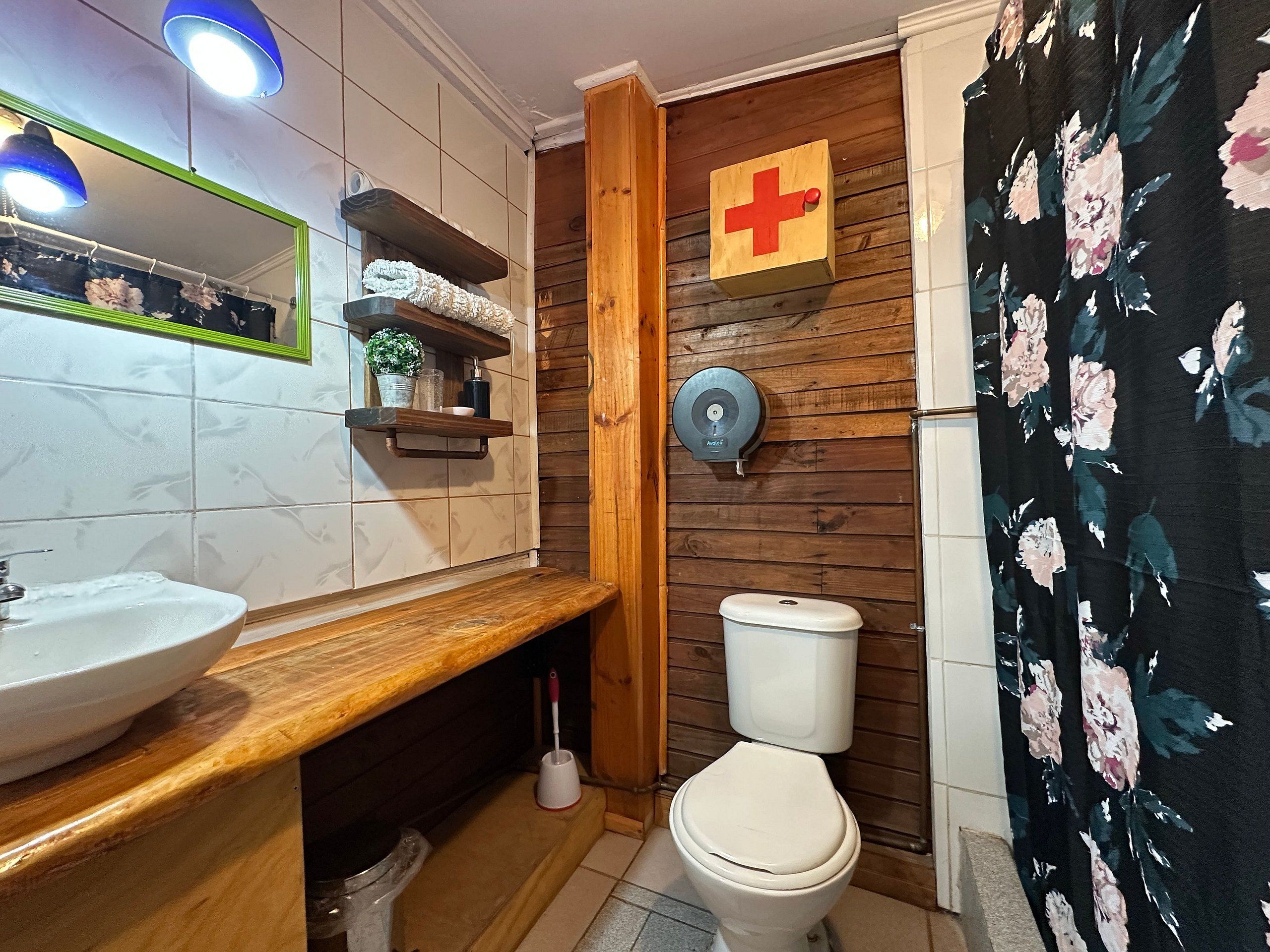 A bathroom with a wooden vanity, a white sink, a toilet, and a shower curtain with a floral pattern.