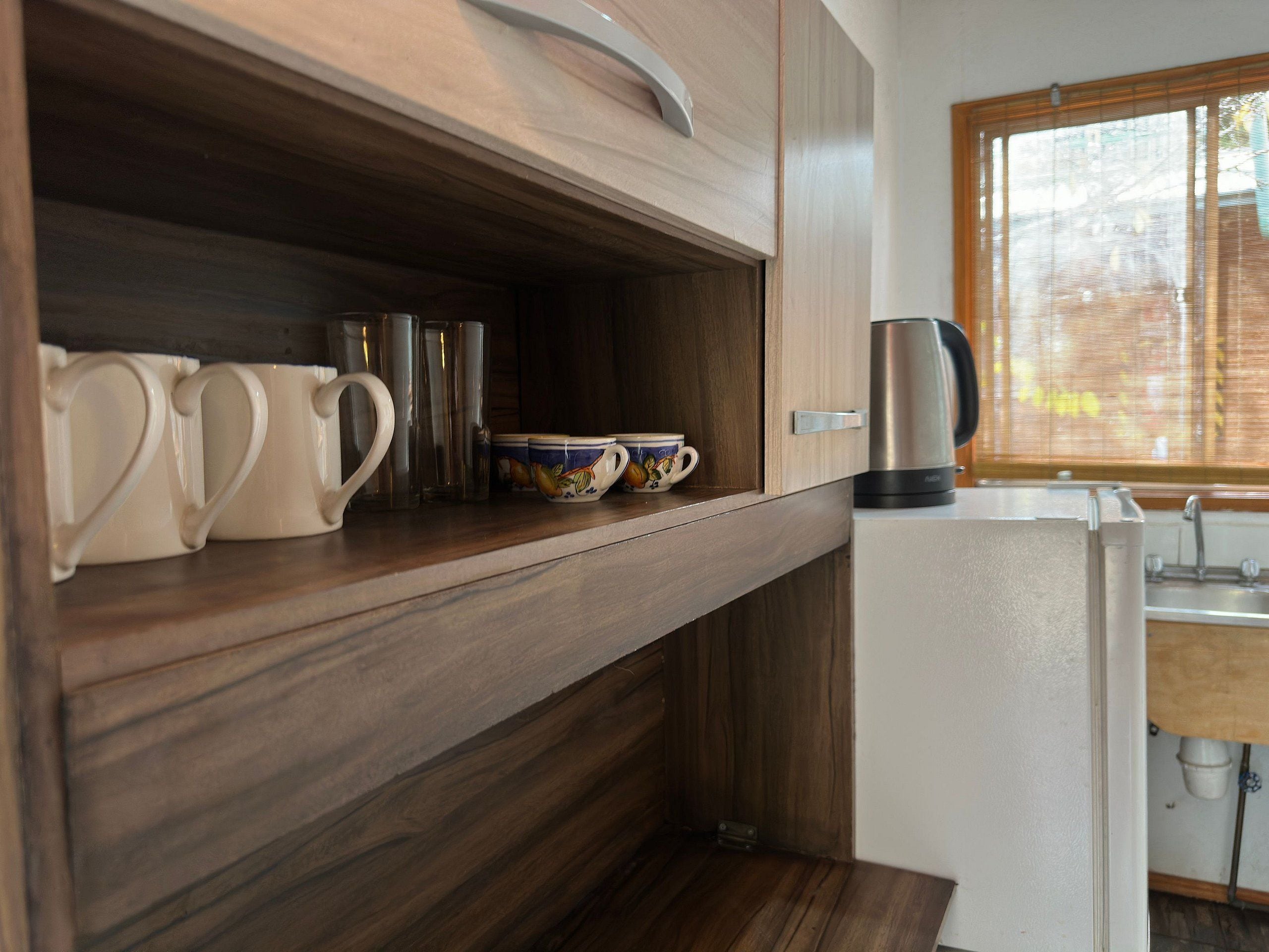 Una cucina compatta con mobili in legno, un bollitore in acciaio inossidabile e una finestra con persiane.