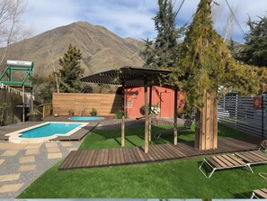 En baghave med swimmingpool, træterrasse og pergola.
