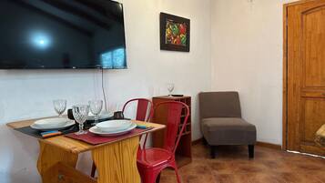 A dining area with a wooden table, red chairs, a television mounted on the wall, and a door to the right.