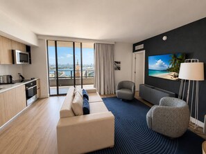 A modern hotel room with a balcony, a sofa, a TV, a lamp, and a kitchen area. - 2 Bedrooms Condo with Balcony & Amazing Views in Downtown (Miami)