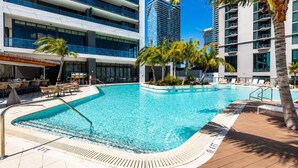 A swimming pool with lounge chairs and palm trees, surrounded by modern buildings. - 2 Bedrooms Condo with Balcony & Amazing Views in Downtown (Miami)