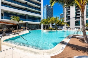 A swimming pool with lounge chairs and palm trees, surrounded by modern buildings. - 2 Bedrooms Condo with Balcony & Amazing Views in Downtown (Miami)