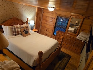 Quarto de cabana de madeira com cama, cômoda e mesa de cabeceira.