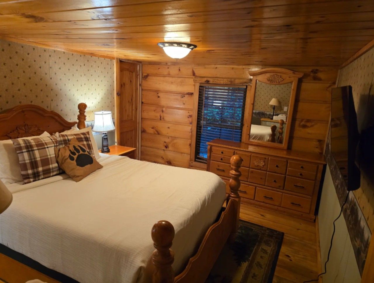 Quarto de cabana de madeira com cama, mesa de cabeceira, cômoda e espelho.