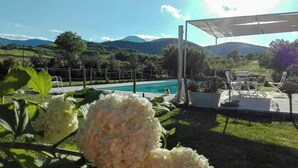 Ein Pool mit Bergblick, umgeben von Grünflächen und einer überdachten Terrasse.