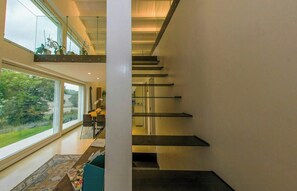 Un intérieur moderne avec un escalier, un coin repas offrant une vue dégagée et une véranda en verre agrémentée de plantes.