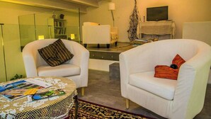 Ein modernes Wohnzimmer mit zwei weißen Sesseln, einem Couchtisch mit Zeitschriften, einem Bücherregal, einem Fernseher und einer Lampe.