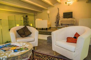 A modern living room with two white armchairs, a coffee table with magazines, a bookshelf, a TV, and a lamp. - Wellness Retreat between Marche and Umbria (Sassoferrato)