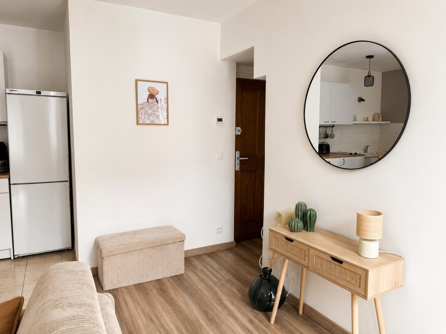 Eine moderne Küche mit Kühlschrank, einer Holzbank, einem Konsolentisch mit Dekoration und einem runden Spiegel an der Wand.