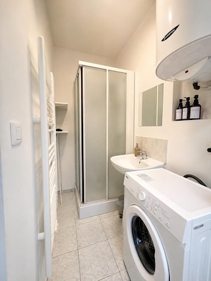 Een moderne badkamer met een douchecabine van glas, een ingebouwd wastafelmeubel en een voorlader wasmachine.