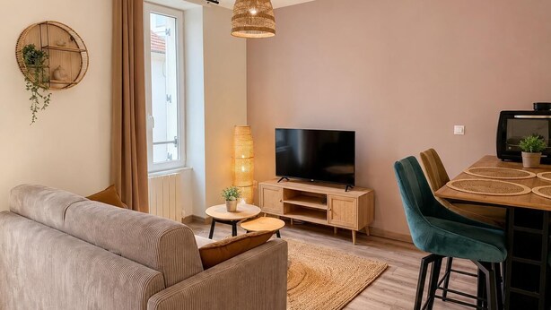 Ein Wohnzimmer mit einer Couch, einem Fernseher, einem Esstisch, Stühlen und einer Lampe.
