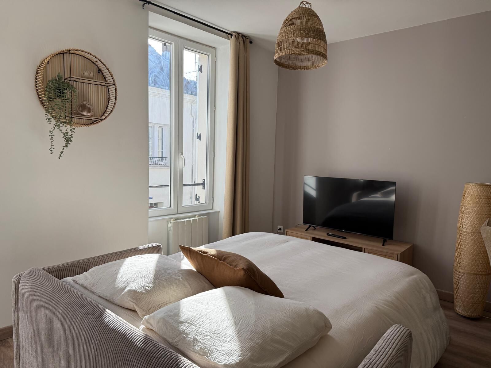 Ein Schlafzimmer mit einem Bett, einem Fernseher, einem Fenster und einer Pendelleuchte.