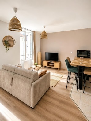 Un salon moderne comprenant un canapé, un téléviseur, une table à manger et des suspensions en rotin.