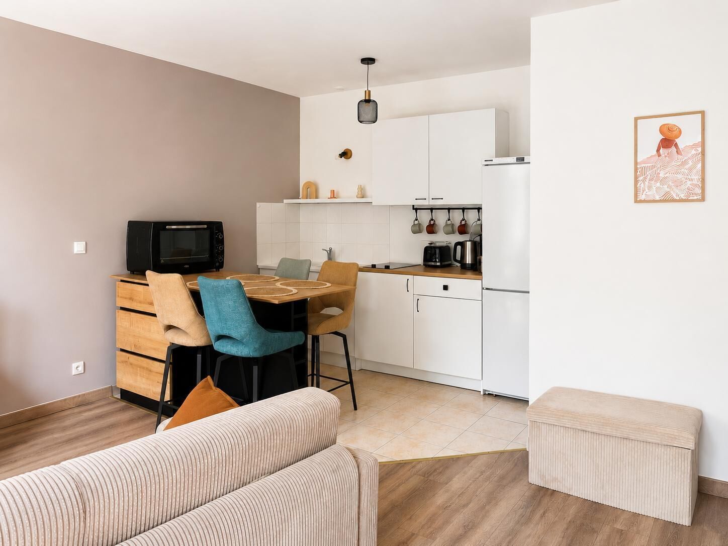 Een compacte woonruimte met een kitchenette, een eethoek met tafel en stoelen, een bank en een klein voetenbankje.