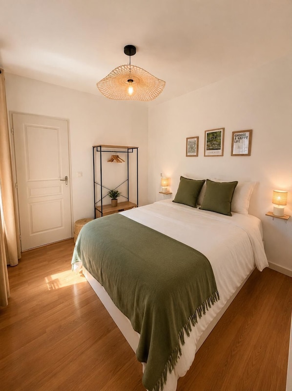 Une chambre à coucher avec un lit, des lampes de chevet, un luminaire suspendu, une porte et des œuvres d’art murales.