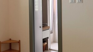 Un couloir avec une porte donnant sur une salle de bain, une petite étagère en bois et une lampe à motifs à carreaux.