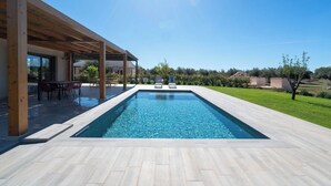 Une piscine rectangulaire dotée d’une terrasse en bois et d’un espace salon abrité.