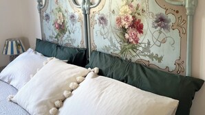 Un lit avec une tête de lit à motifs floraux, un oreiller blanc orné de glands et un oreiller vert.