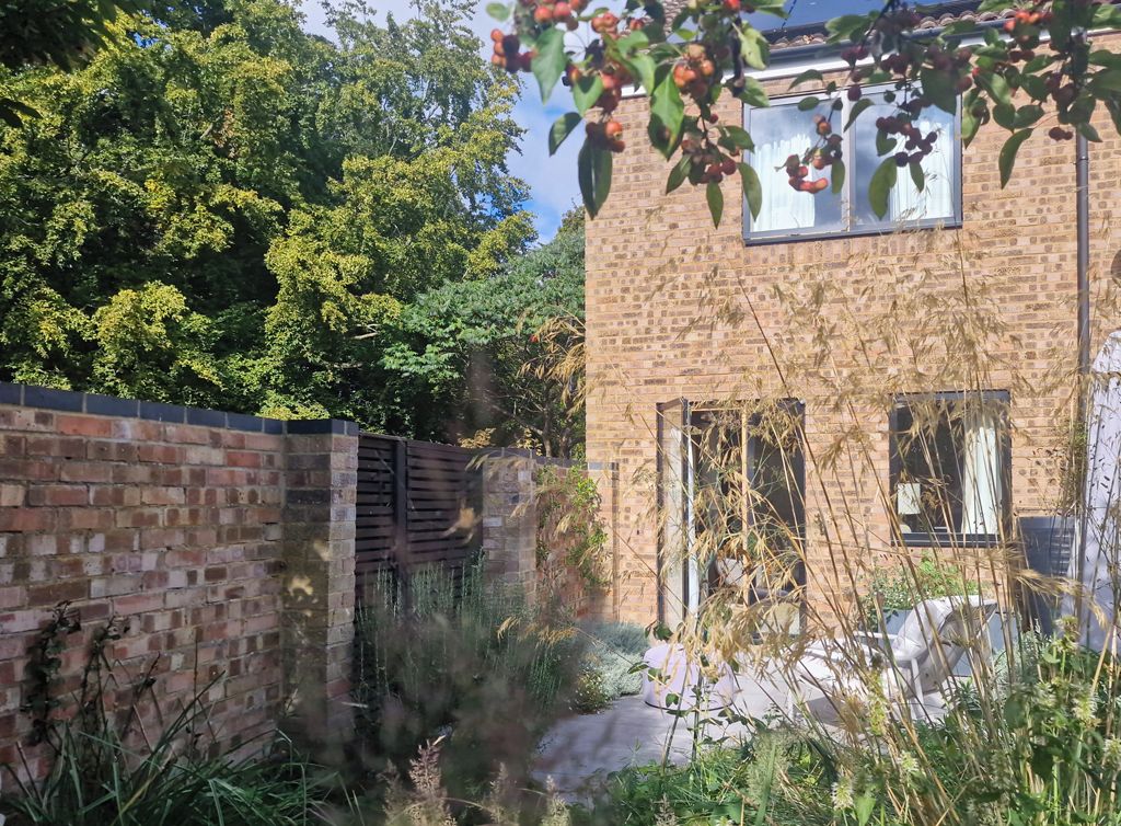 A brick building with a window and a door, surrounded by greenery and a brick wall.