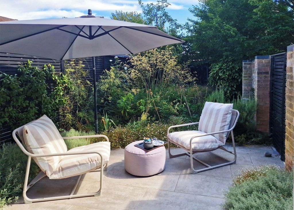 An outdoor patio with two cushioned chairs, a round ottoman, and a large umbrella.