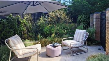 An outdoor patio with two cushioned chairs, a round ottoman, and a large umbrella.
