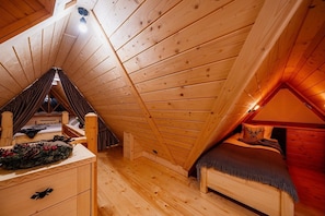 A cozy attic bedroom with a sloped ceiling, wooden walls, a bed with a headboard, a dresser, and a small table with a decorative wreath. - A Large Mountain-style House With a spa Area (Poronin)