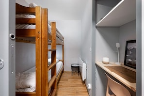 Une petite pièce avec des lits superposés, un bureau, une chaise, un radiateur et un tableau encadré au mur.
