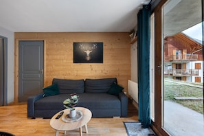 Un intérieur moderne avec un mur en bois, un canapé gris, une petite table ronde ornée d’une plante et un tableau représentant un cerf.