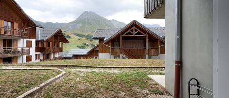 A wooden building with a balcony, a grassy area, and a mountain in the background.